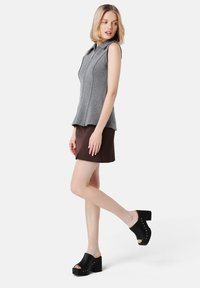 Gray sleeveless top with a collar and front zipper, paired with a brown skirt. Black platform clogs with decorative studs complete the outfit.