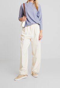 Ljusblå stickad tröja med ribbat mönster, krämfärgade vida byxor och beige sneakers. Vit axelväska med kedjerem.