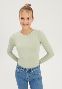 Long-sleeve mint green top with a round neckline, fitted design, and soft texture, paired with blue high-waisted jeans.