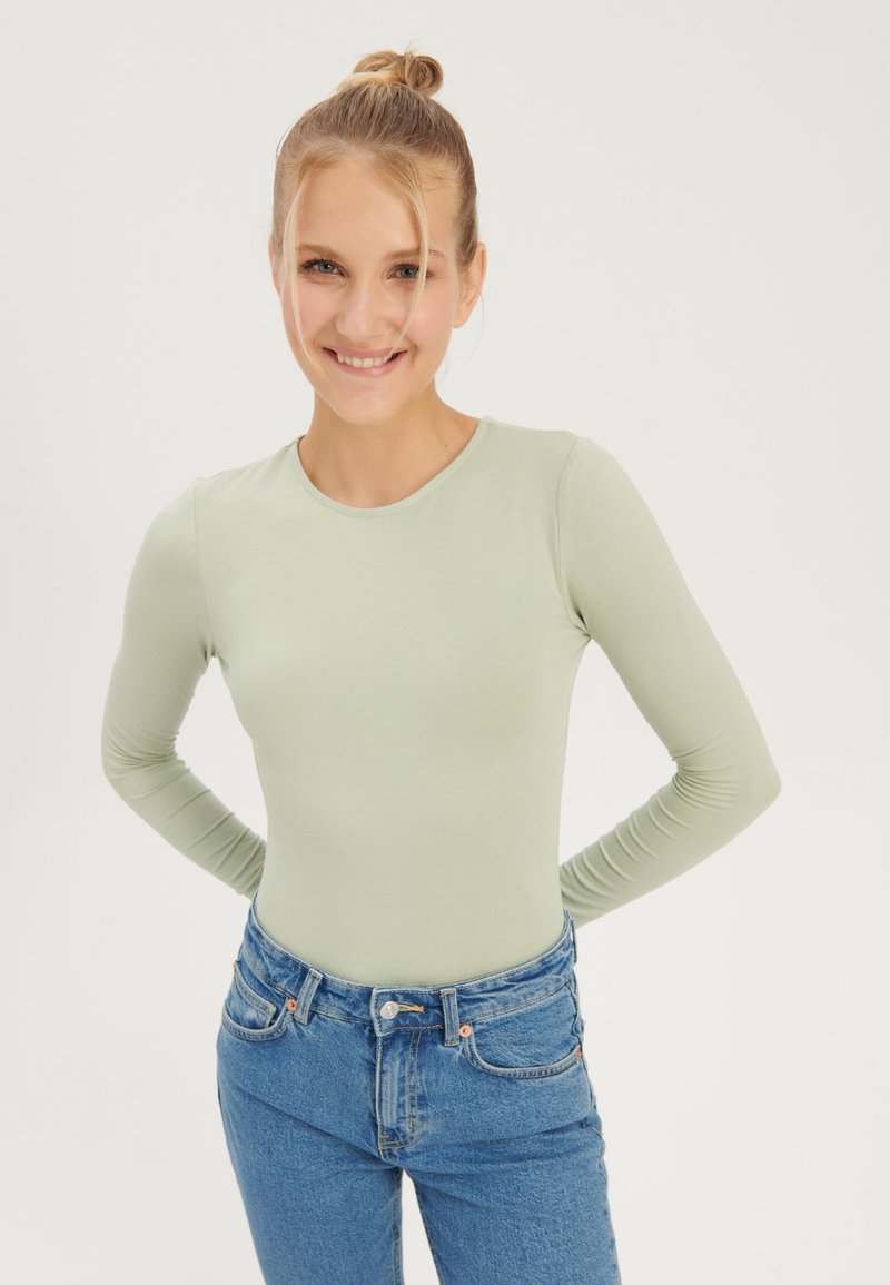 Long-sleeve mint green top with a round neckline, fitted design, and soft texture, paired with blue high-waisted jeans.