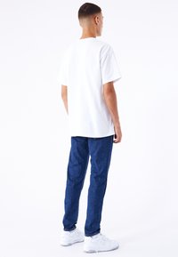 Camiseta blanca de algodón, corte relajado, combinada con pantalones de mezclilla azul. Presenta una textura suave y un diseño minimalista. Calzado: zapatillas blancas.