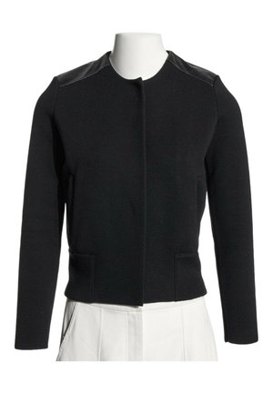 Veste noire à manches longues avec des panneaux en cuir aux épaules et sans boutons visibles, présentée sur un buste de mannequin blanc portant un pantalon blanc.