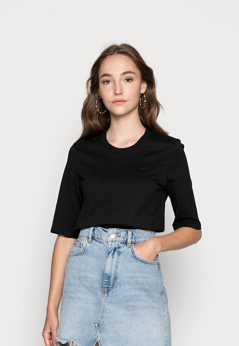 Svart bomulls T-skjorte med korte ermer og rund hals, med en liten logo på brystet, kombinert med en lys blå denimskjørt.