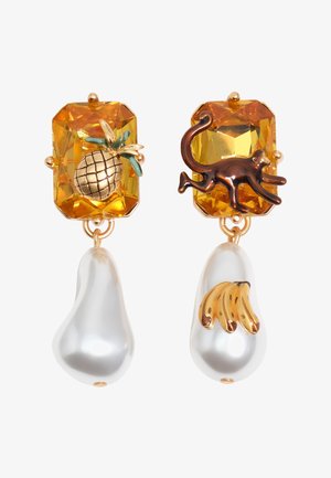 Asymetryczne kolczyki z bursztynowymi kamieniami; jeden przedstawia złotego ananasa i biały kroplę, drugi brązowego kota i białą kroplę ze złotymi bananami.