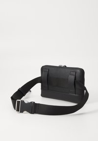 Černá kožená taška s texturovaným povrchem, vybavená odnímatelným popruhem a dvěma textilními držadly; obdélníkový tvar se zipovým uzávěrem.