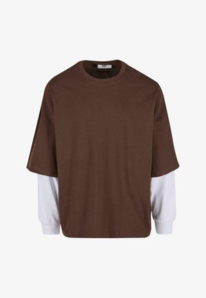 Camiseta marrón de gran tamaño con cuello redondo y mangas cortas, superpuesta sobre mangas largas blancas; tela de algodón, con un estilo minimalista.