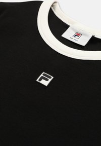 Chemise noire avec col rond blanc et petit logo carré avec un "F" stylisé en noir sur la poitrine, sous l'étiquette du col.