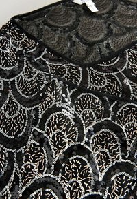 Juodas blizgus audinys su bangų raštu, papuoštas sidabrinėmis ir smėlio spalvos detalėmis. Minkšta tekstūra su blizgančiais, atspindinčiais paviršiais.