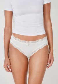 Weiße Unterwäsche mit Spitzenbesatz, aus einem glatten Stoff, mit floralen Details am Rand und einem kleinen Schleifenakzent in der Mitte vorne.