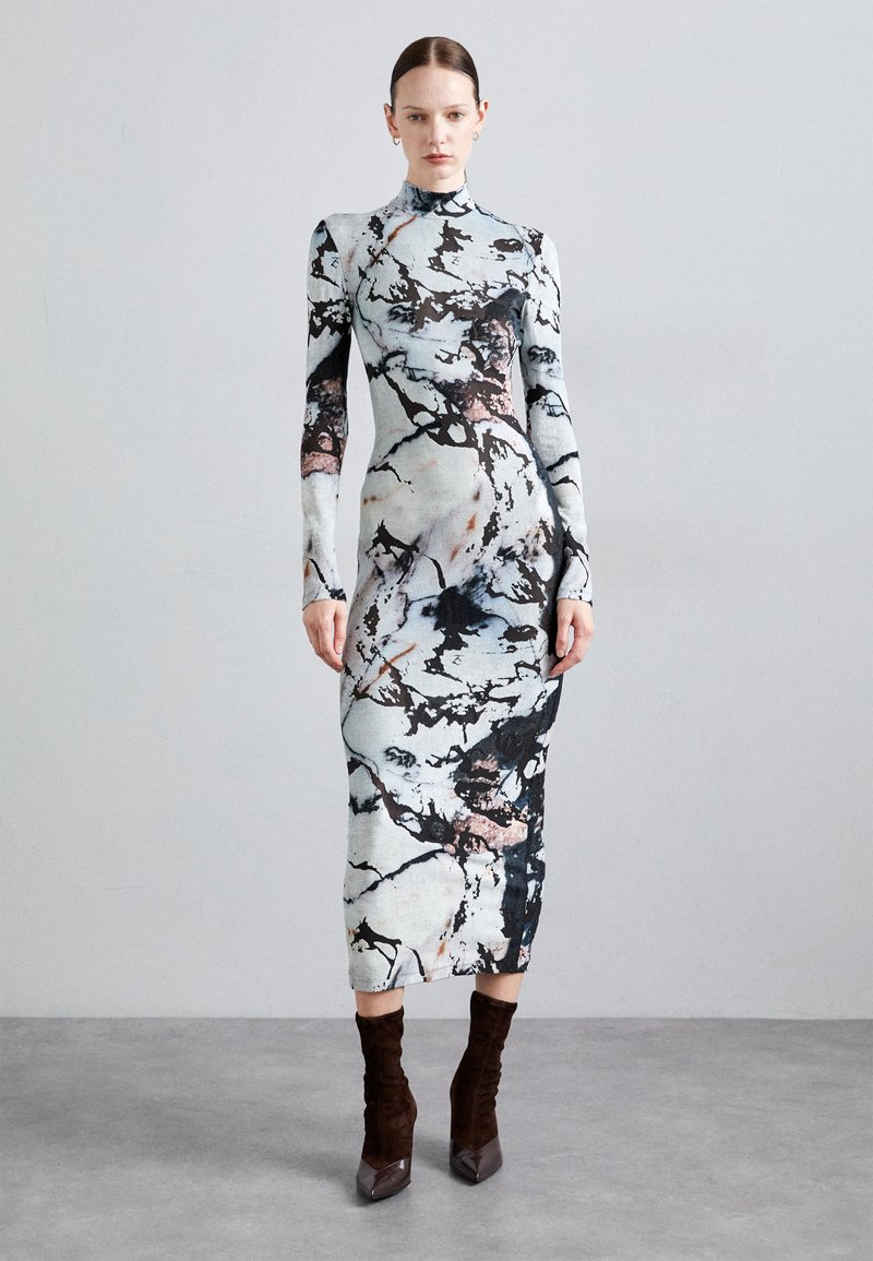 Form-fitting, long-sleeve dress in a light blue and black marble print. High neckline, mid-calf length, textured fabric, paired with brown ankle boots.