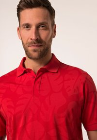Červené polo tričko s jemným vzorem listů, krátké rukávy a dvouknoflíkovou légu. Vyrobeno z lehké tkaniny s hladkou texturou.