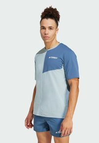 Maglietta sportiva a maniche corte di colore azzurro chiaro e blu scuro con un design geometrico; tessuto morbido; presenta il logo TERREX sul petto.