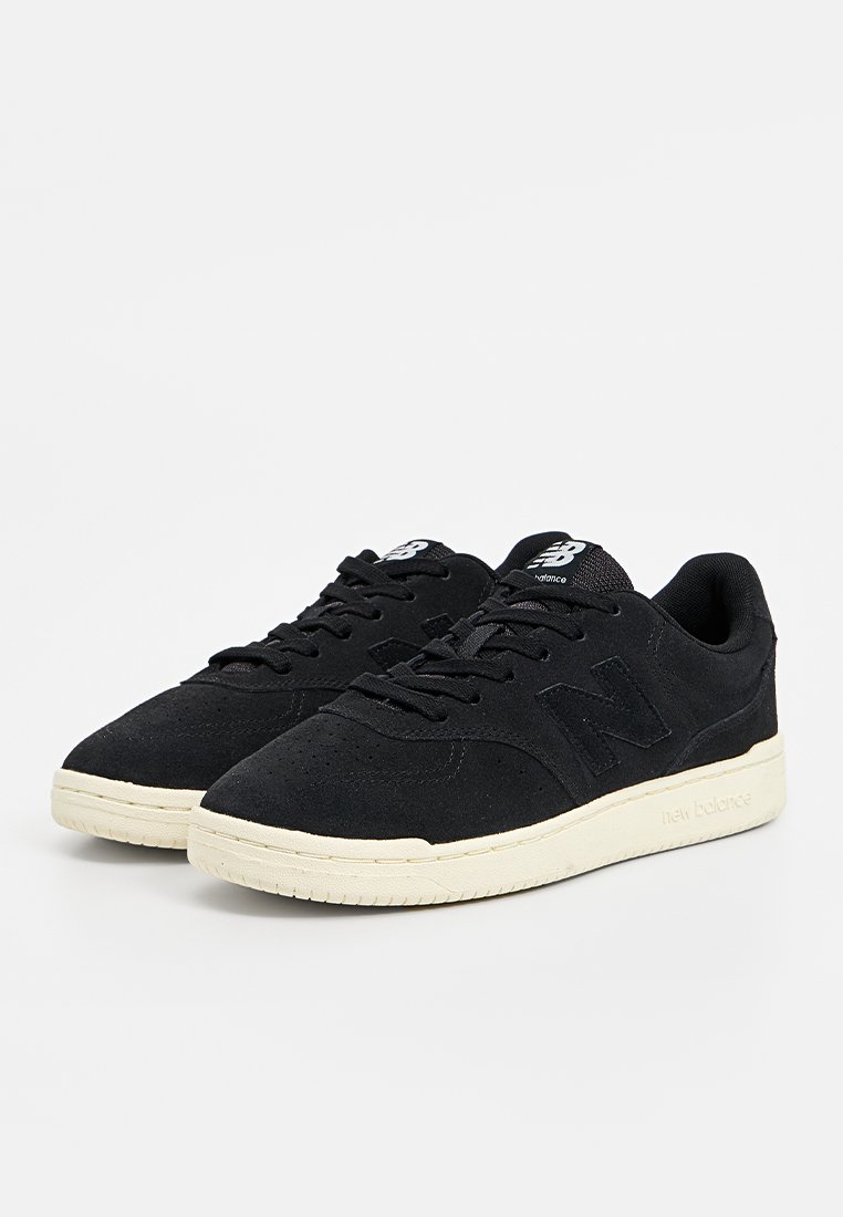 Zwarte nubuck sneakers met een afgeronde neus, platte vetersluiting, rubberen zool en witte accenten op de zool en branding.