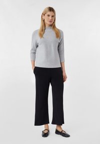 Grijze gebreide trui met een hoge hals, driekwartmouwen, gecombineerd met losse zwarte broek en platte zwarte schoenen.