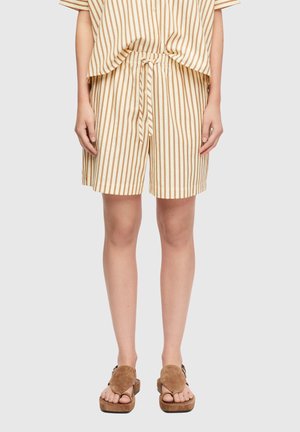 Osoba ubrana w beżowe i brązowe szorty w pionowe paski z dopasowanym topem oraz brązowe zamszowe sandały na platformie, stoi na jednolitym tle.