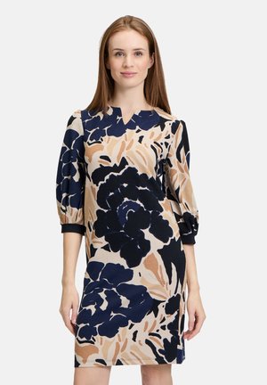 Abito floreale con un motivo blu navy, beige e nero. Presenta una silhouette aderente, maniche a tre quarti e un dettaglio con scollatura a V.