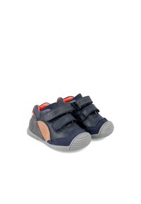 Zapatillas infantiles de color azul marino con dos correas de Velcro, detalles en color beige, suela de goma gris y paneles laterales perforados. Tienen un acabado de cuero suave y un cuello acolchado.