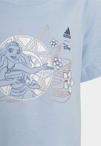 Ljusblå bomullströja med grafik av en karaktär, blommönster och varumärkeslogotyper i marinblått och korall. Kort ärm och rundad hals.