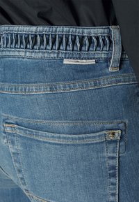 Modré džínové kalhoty s nařaseným elastickým pasem, zadními kapsami a klasickým pětipocketovým designem s kontrastním šitím.