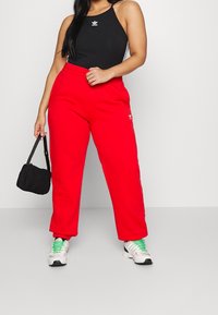 Röda träningsbyxor med elastiskt midjeband, sidfickor och vitt logotyp. Kombinerat med en svart halterneck-top och svart väska. Sneakers med vita detaljer.