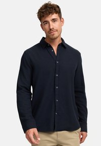Camisa de manga larga azul marino hecha de tejido ligero, con cuello abotonado, botones en la parte delantera y una textura suave.