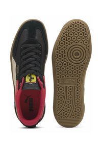 Sort og beige Puma Palermo sneakers med rød krave, sorte snørebånd, Ferrari logo på tungen og gummisål, der viser et cirkulært dækmønster.