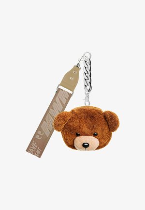 Llave en forma de oso de peluche marrón, hecha de material suave, con ojos negros y un hocico beige. Se sujeta con una cadena metálica y una correa beige.