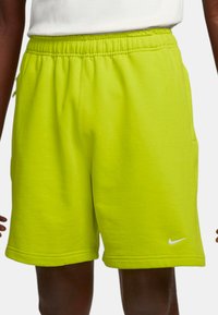 Zelené bavlněné šortky s elastickým pasem, bočními kapsami a malým bílým logem Nike v dolním levém rohu. Měkký materiál.