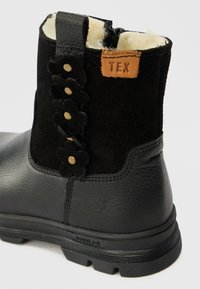 Czarne skórzane i zamszowe botki za kostkę z piankowym wykończeniem, szczegóły w kwiaty na pasku oraz brązową etykietą "TEX" przy górnej części.