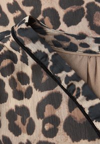 Leopardprintstof med farver i beige, brun og sort. Tekstureret overflade med en let glans. Buet halsudskæring med sort kant.