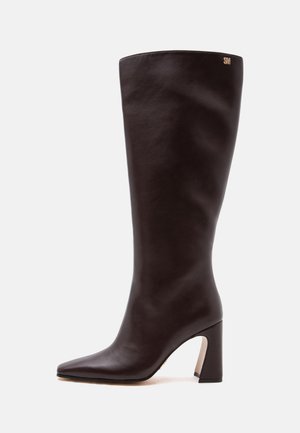Tall dark brown leather boot with a pointed toe and block heel, featuring a small gold logo near the top edge.
