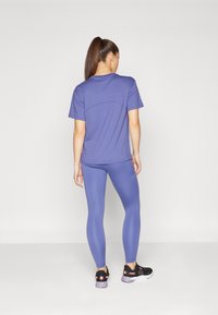 T-shirt de sport violet et leggings assortis, design ajusté avec une texture lisse. Des baskets noires avec des accents roses complètent le look.