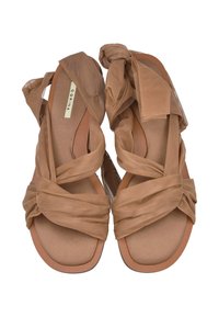 Sandalias marrones con correas de tela cruzadas y acentos de lazo. La suela es plana y texturizada, con un forro interior suave para mayor comodidad.