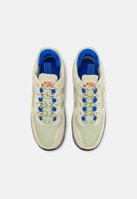 Nike-sneakers i ljusgrön och blå. Har en texturerad tyg, snörningsdesign och orange logotyp. Rundad tå med en kontrasterande sula.