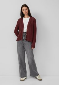 Cárdigan de punto burdeos con cinco botones, escote redondo y mangas largas, combinado con jeans de pierna ancha grises de cintura alta y zapatillas.