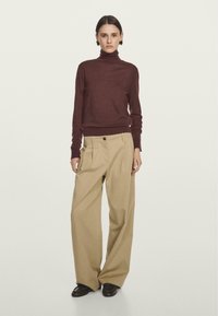 Burgundský rolák s upnutými manžetami, kombinovaný s volnými, světlými kalhotami s vysokým pasem, které mají př oversized kapsou a detailem s knoflíky.