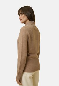 Maglione beige a collo alto con maniche lunghe, texture morbida e forma aderente, abbinato a pantaloni in corduroy color crema.