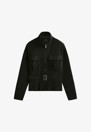 Geacă neagră cu mâneci lungi, fermoar și guler înalt, două buzunare mari pe piept cu clapete și talie cu curea și cataramă argintie.