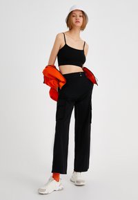 Zwarte cropped tanktop, oversized oranje jasje, zwarte cargo broek met zakken, witte sneakers en oranje sokken. Soepele texturen en casual ontwerp.