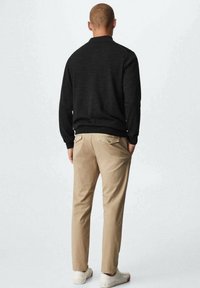 Czarny sweter, beżowe spodnie i białe trampki. Sweter ma gładką fakturę, spodnie posiadają tylne kieszenie, luźny krój, monochromatyczna kolorystyka.