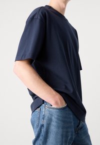 Mörkblå bomullströja med korta ärmar, rundad halsringning och avslappnad passform, kombinerad med ljusblå denimjeans.