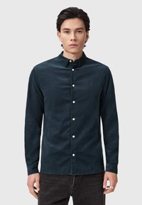 Camicia di velluto a coste blu navy con maniche lunghe, colletto button-down, bottoni bianchi e ricamo discreto sul petto. Texture liscia, vestibilità sartoriale.