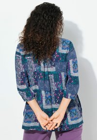 Multifarvet bluse med et patchworkdesign i nuancer af blå, lilla og grøn. Har trekvartærmer og en afslappet pasform.