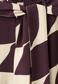 Material violet închis și crem cu model abstract curbat legat într-un nod, evidențiind textură și căderea materialului.