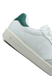 Valkoinen nahkainen tennari, jossa vihreä kantapääkoriste, teksturoitu kumipohja, sivussa rei'itetty logoyksityiskohta ja yksinkertainen nauhakiinnitys.