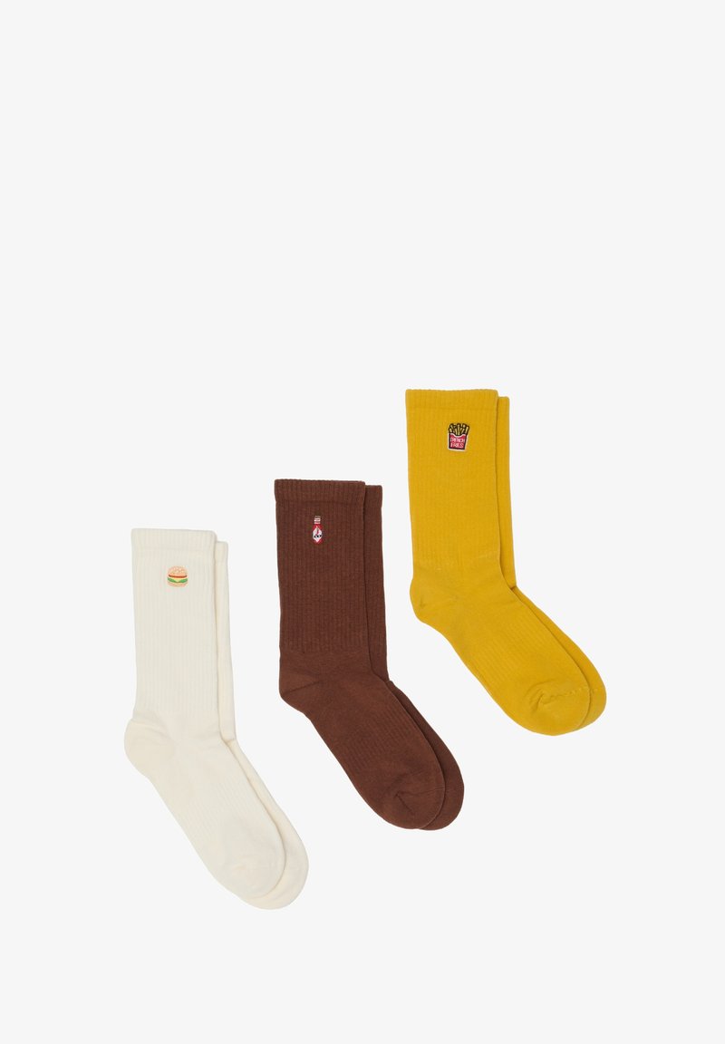 Tres pares de calcetines: blancos con un diseño de hamburguesa, marrones con una botella de ketchup y amarillos con patatas fritas, todos con textura acanalada.