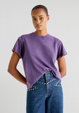 T-shirt violet à col ras du cou avec des manches retroussées, fabriqué dans un tissu doux. Assorti à un jean taille haute bleu avec des rivets argentés le long des poches.