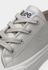 Κοντινό πλάνο γκρι αθλητικού παπουτσιού Lee με χοντρές κορδόνια, μεταλλικά οφθαλμάκια με τη σήμανση "Lee 1889" και εμφανές λογότυπο στη γλώσσα.