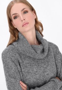 Grau gestrickter Pullover mit breitem Schalkragen und langen Ärmeln. Der Stoff wirkt weich und warm und zeigt ein dezentes, abwechslungsreiches Muster.
