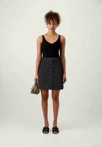 Fekete ujj nélküli felső, szürke gombos szoknya és fekete csúszó szandál. Textúrált szoknya, amely fitted sziluettel és oldalsó zsebekkel rendelkezik. Kis kézitáska.